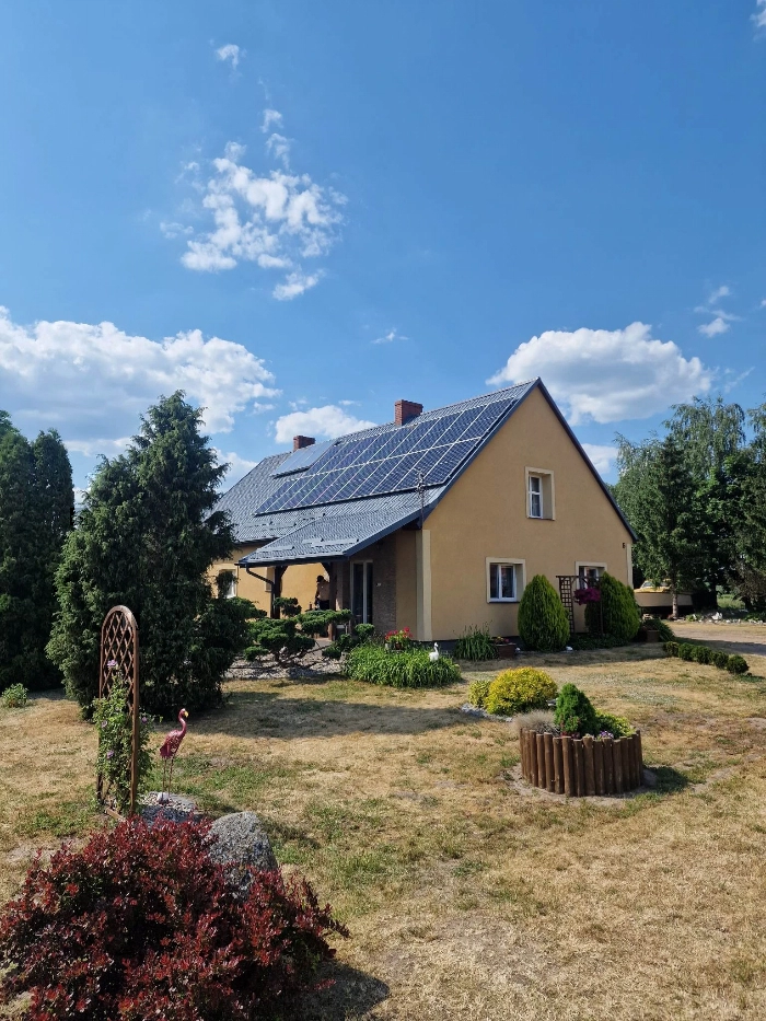 Instalacja fotowoltaiczna na żółtym domku jednorodzinnym na tle czystego nieba i słońca.